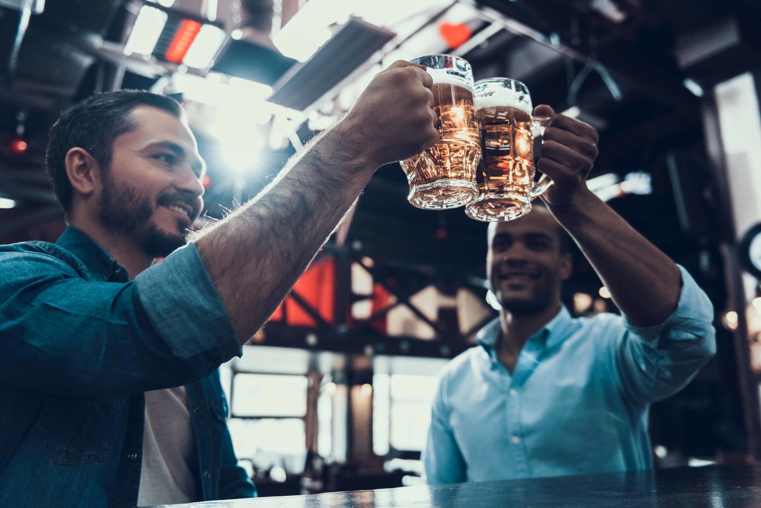 Two men with glasses of beer clink their drinks together