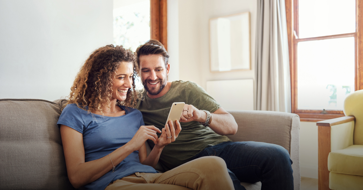 A man and a woman sit down on the sofa, reading an article on a mobile phone about 'What is a current account?'