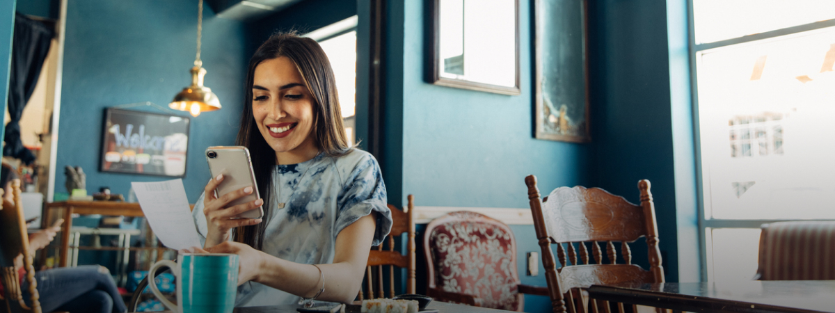 A lady sits down at the table and looks at her phone. There are framed pictures in the background