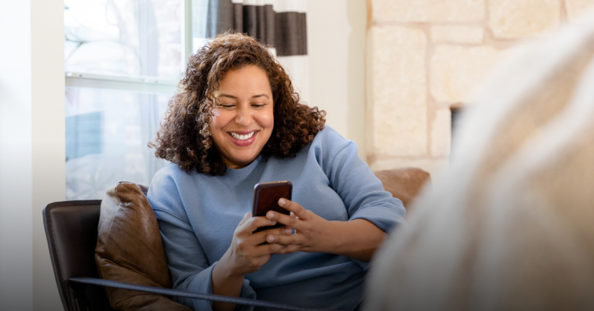 A woman sits on the sofa, holding her phone and reading an article about Wise vs Western Union