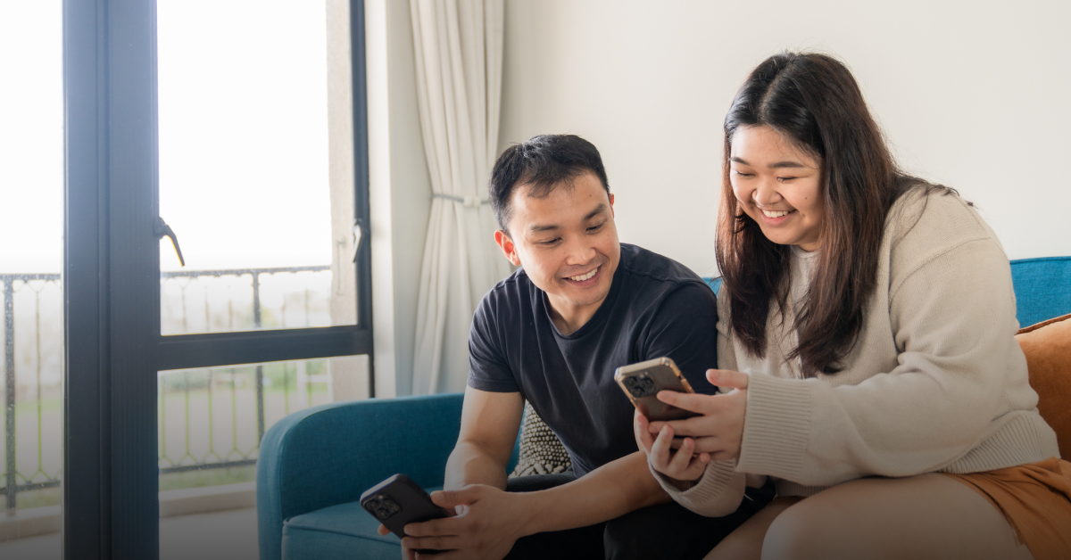 A man and woman sit on a sofa and look at a device as they navigate the cost of living in the Phillippinees