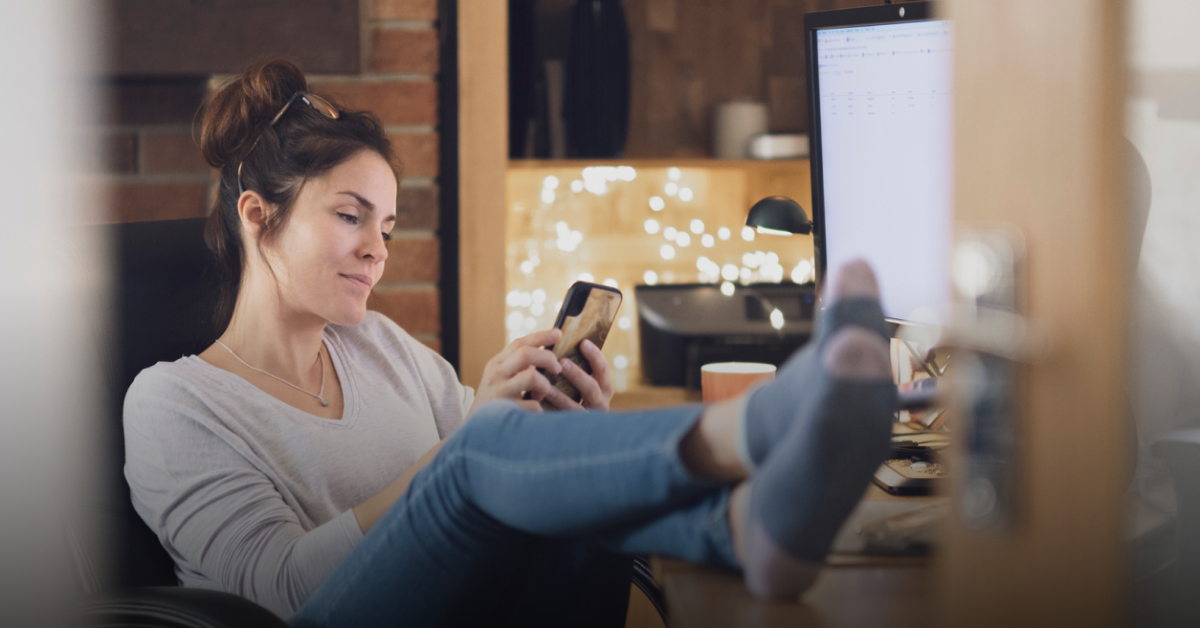 A woman sits with her feet up on the table reading an article on her mobile about Nationwide international transfers