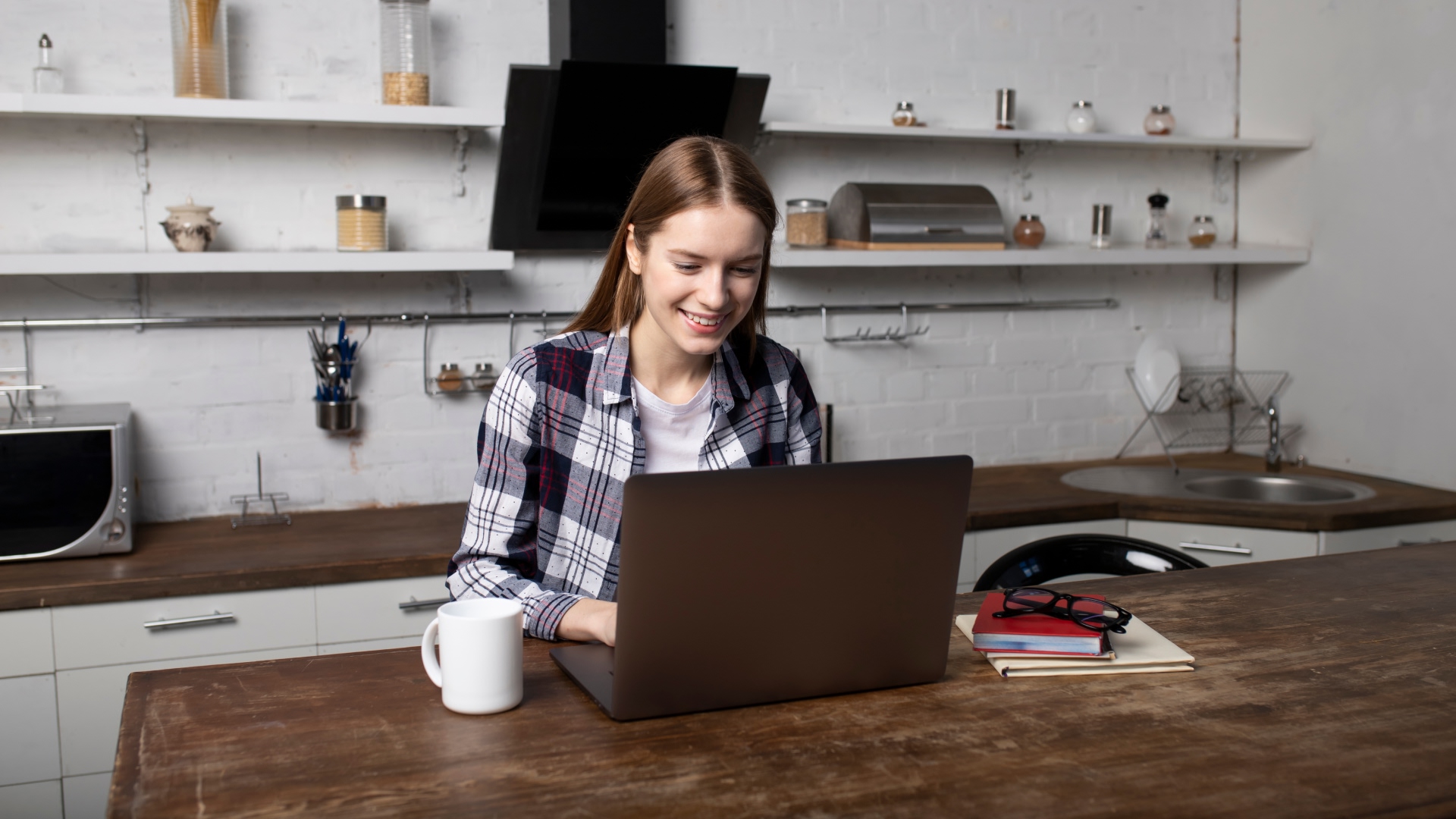 A young female sits at the table reading an article on her laptop about TransferGo vs PayPal Business