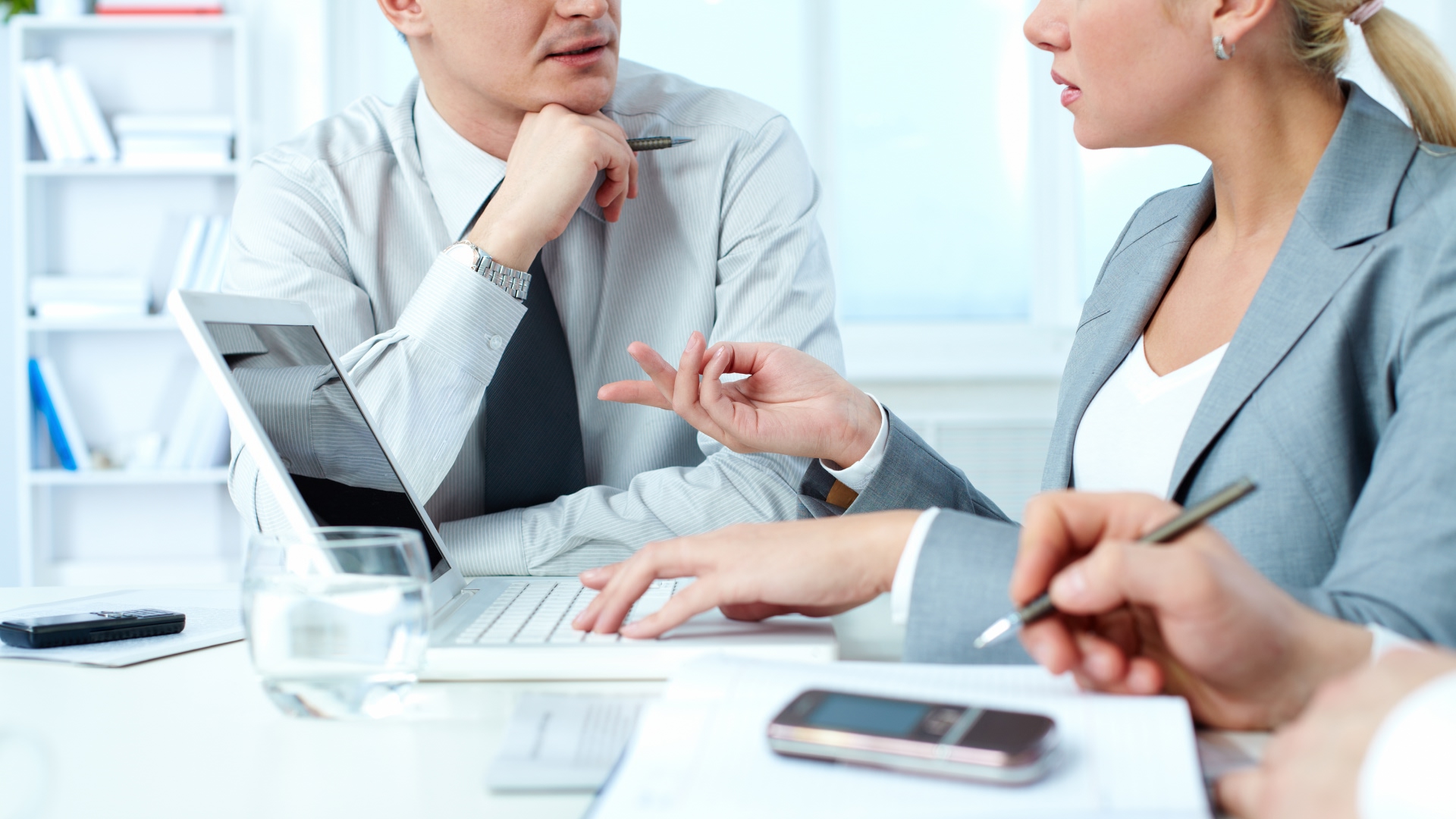 A man and woman in smart office clothing sit at a desk and discuss the question, 'Is Lloyds Business safe?'