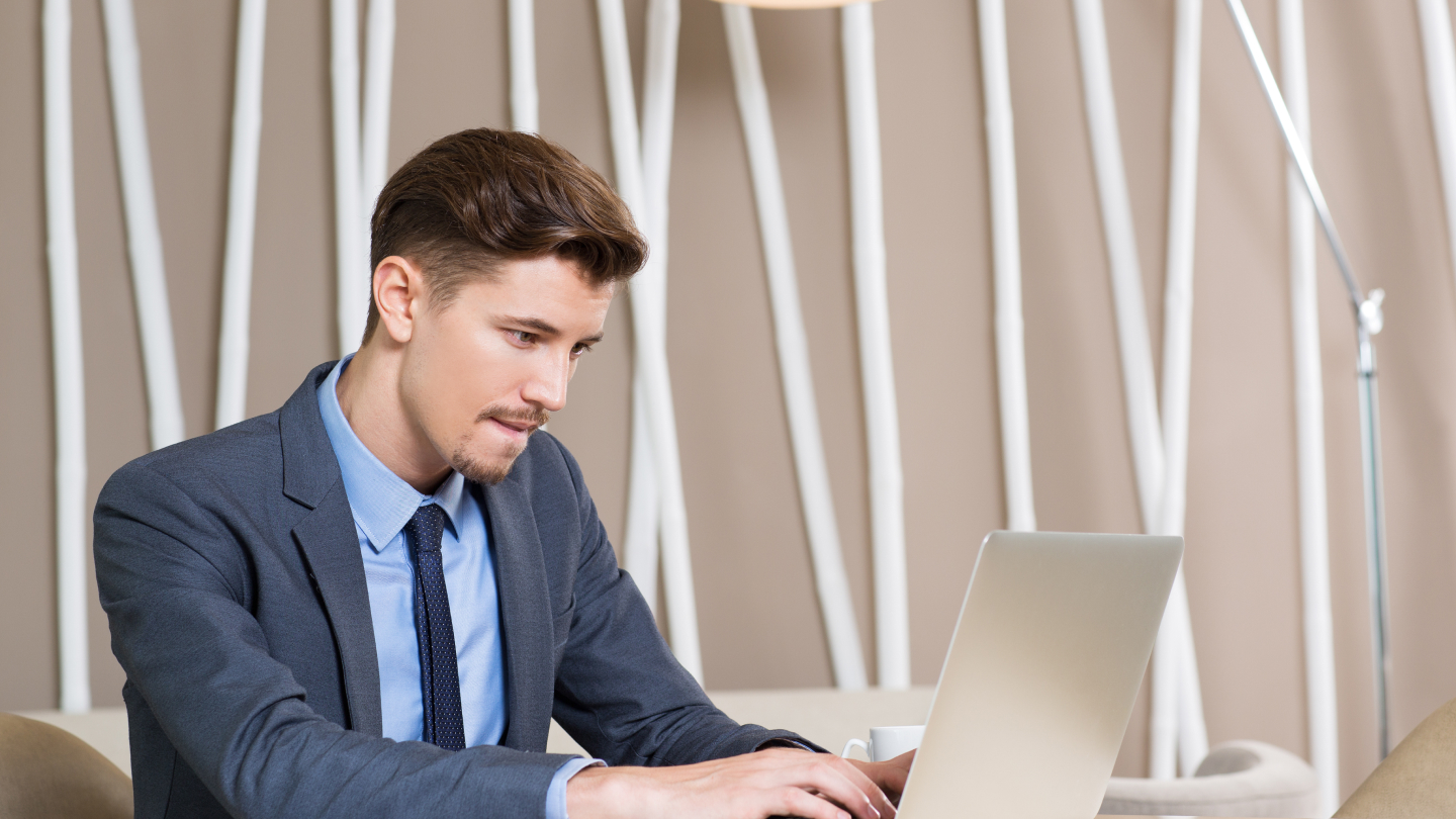 A man in a suit sits at a table on a laptop, beginning his application for a lithuania business visa