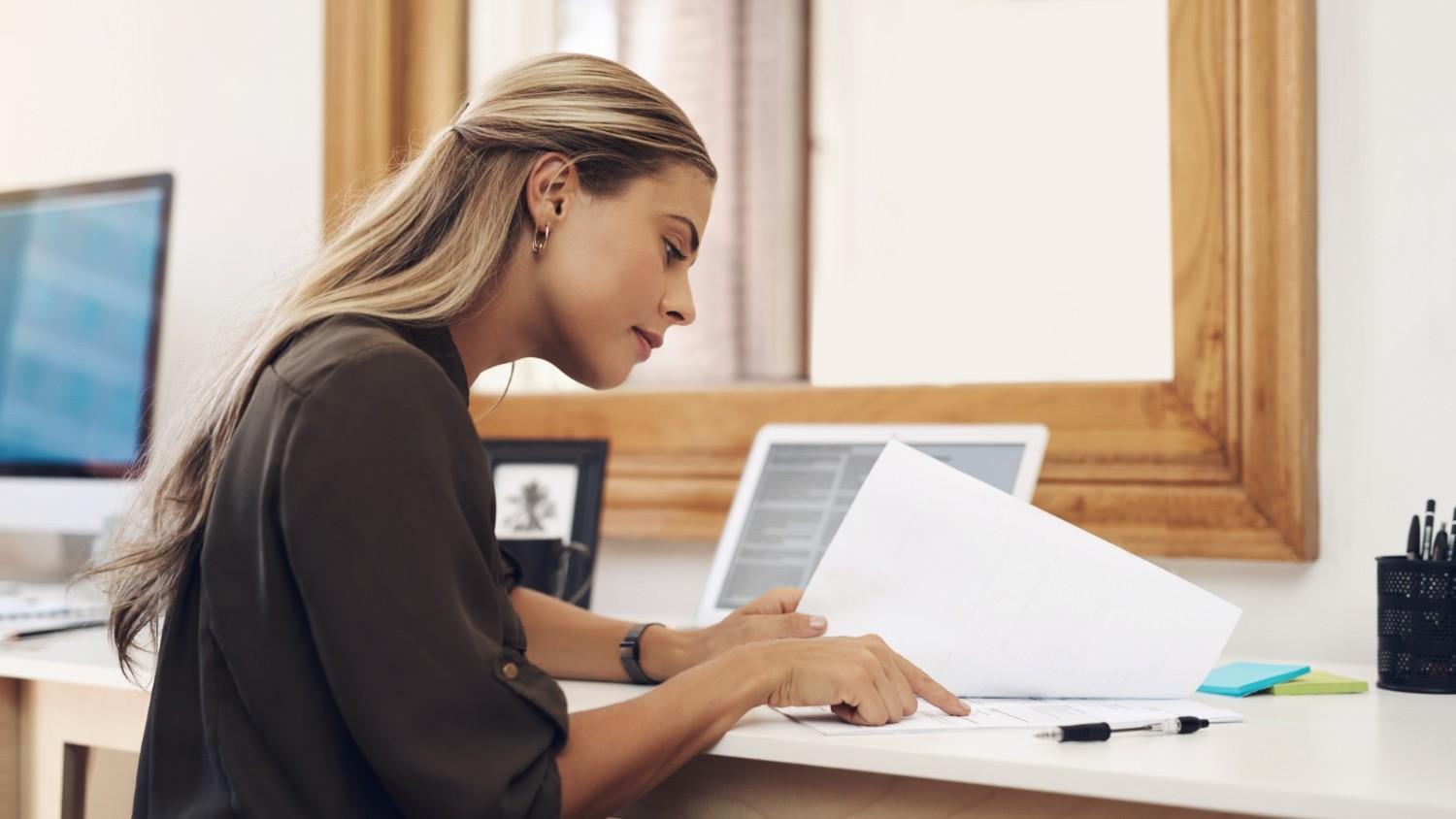 A young, blonde female entrepreneur sits at a desk, reading a guide on the 'register company Lithuania' process