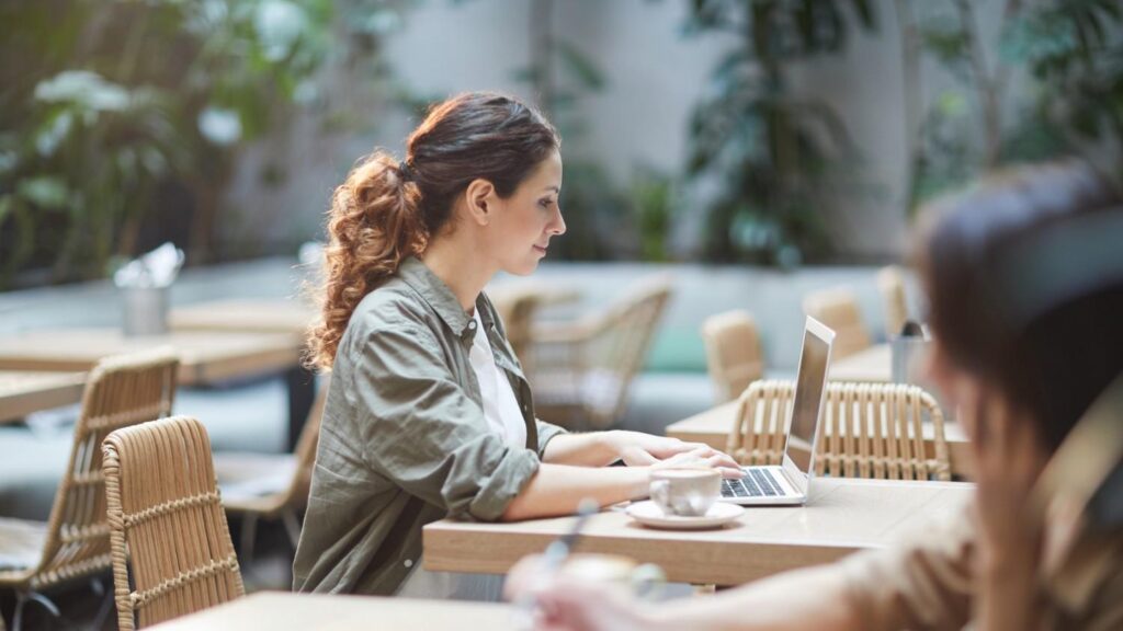 A young brunette female sits at an outdoor table in a cafe, reading an article on Lithuanian business culture