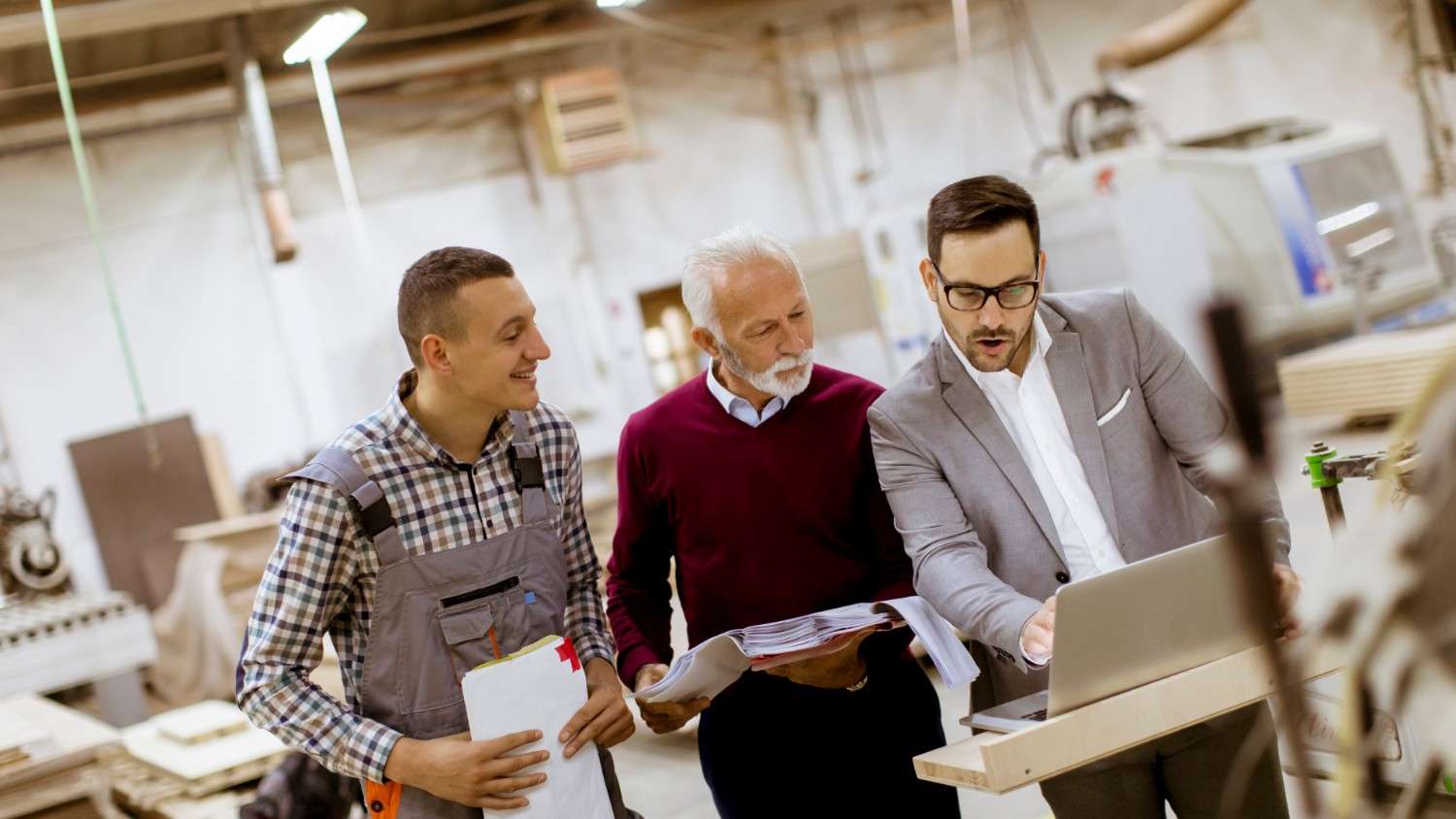 Three men stand together while looking at a laptop, demonstrating collaboration—one of the key components of Lithuanian Business Culture