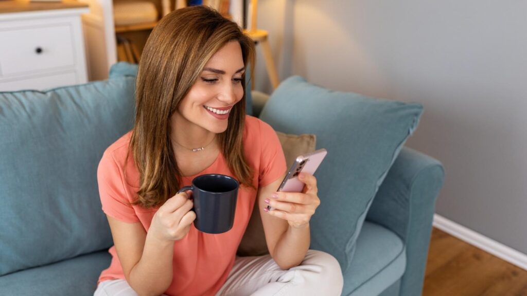 A young brunette female sits on the sofa with a mug of tea, reading an article about the Wise business account