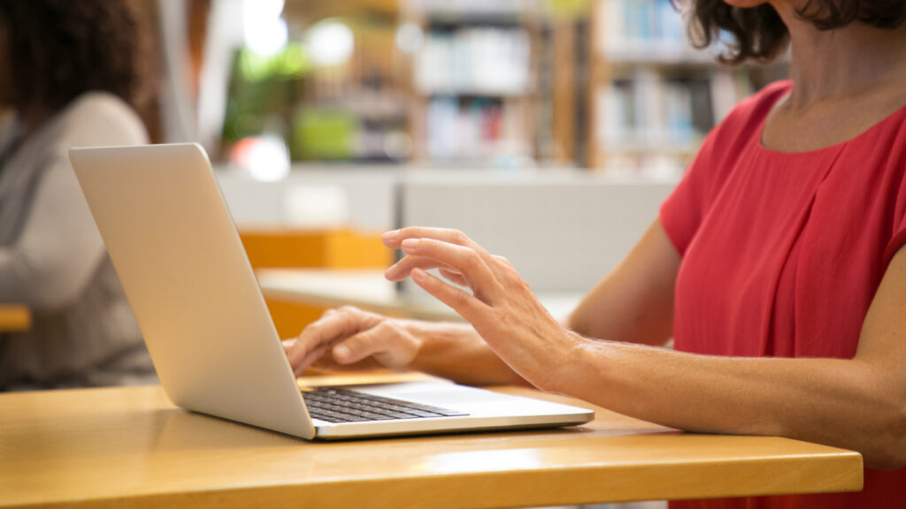 A lady in a red top sits at a table and types on her laptop, beginning her application for a Lithuania Startup Visa