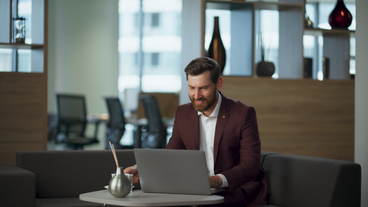 A young white male sits at a desk with his laptop, reading an article on applying for a Lithuanian Startup Visa