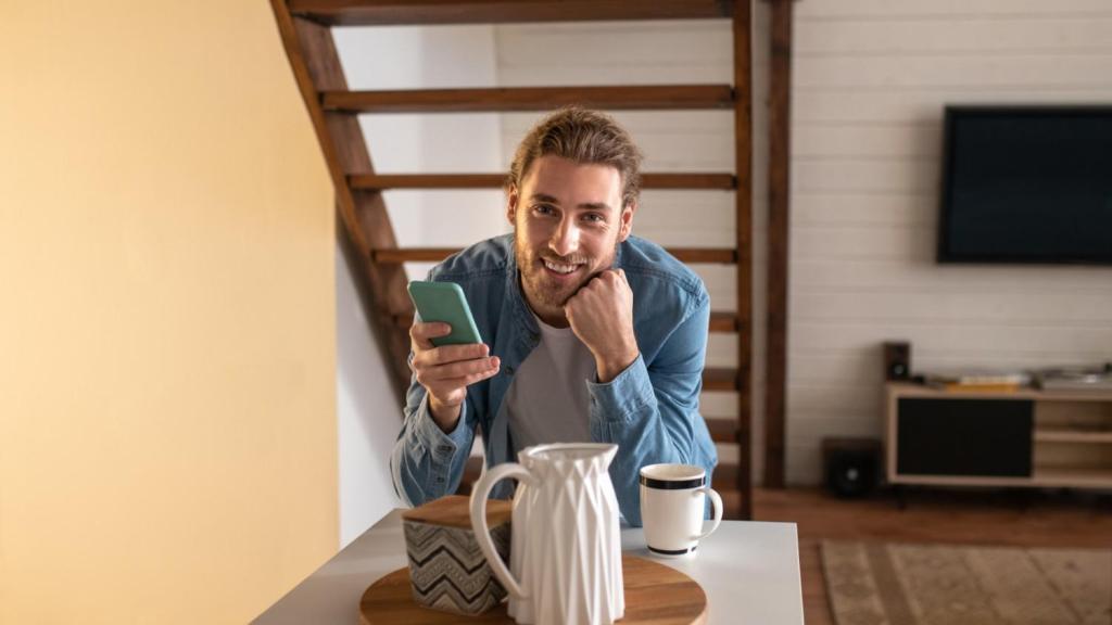 A young man in a blue shirt smiles at the camera, whilst reading an article on his mobile about TransferGo vs SEB Business